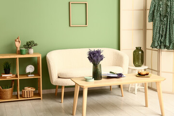 Interior of stylish living room with folding screen, shelving unit, sofa, table and beautiful lavender flowers