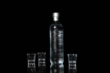 Shots and bottle of cold vodka on black background