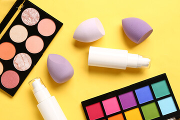 Composition with decorative cosmetics and makeup sponges on yellow background