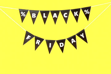 Flags with text BLACK FRIDAY and percent signs hanging on rope against yellow background