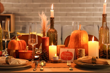 Festive table setting with burning candles, pumpkins and greeting cards for Thanksgiving Day at evening