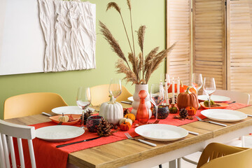 Autumn table setting with pumpkins, dry leaves and burning candles in dining room