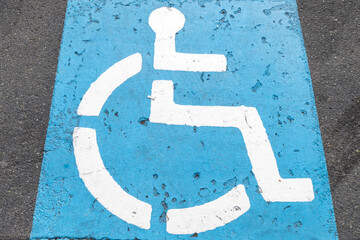 Close-up view of a blue disabled parking sign painted on textured asphalt. The iconic symbol is...