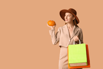 Young woman in autumn clothes with shopping bags and pumpkin on brown background