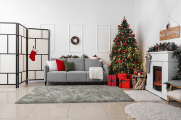 Interior of living room with glowing Christmas tree, sofa and fireplace