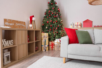 Interior of living room with glowing Christmas tree, shelf unit and sofa
