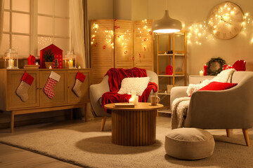 Interior of living room with armchairs, Christmas decor and glowing lights at night