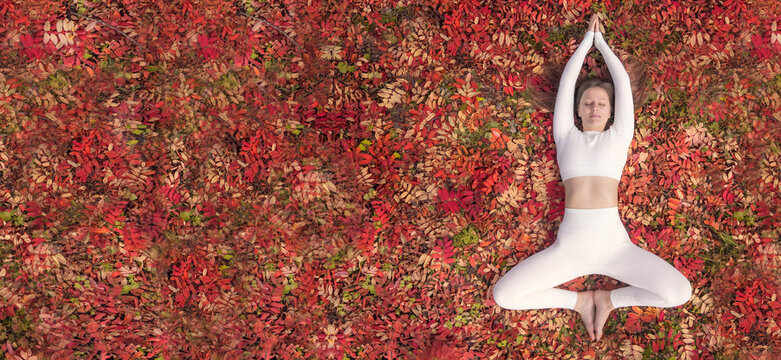 Woman practicing yoga in a serene autumn setting surrounded by vibrant leaves. A woman is engaged in health and fitness on a carpet of red leaves autumn flat lay