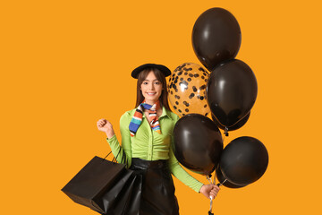 Stylish young woman with shopping bags and balloons on yellow background. Black Friday Sale