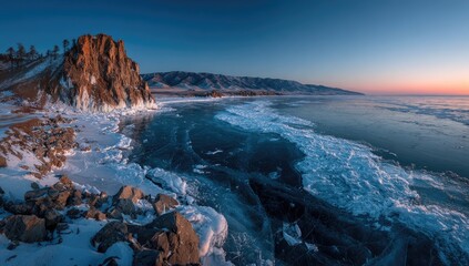 Frozen lake shore at dawn.  Rocky cliffs meet ice-covered water under a vibrant sunrise