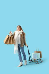 Pretty young woman with shopping bags and sledge on blue background