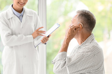 Fototapeta premium Mature man with hearing aid visiting doctor in clinic