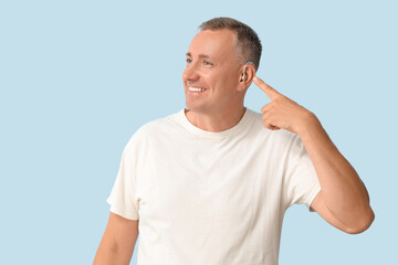 Obraz premium Mature man pointing at hearing aid on blue background