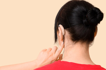 Fototapeta premium Mature woman pointing at hearing aid on beige background, back view