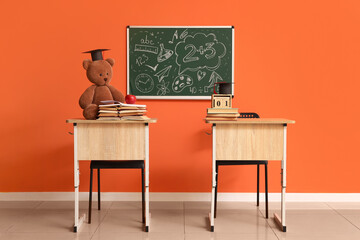 Desks with toy bear, graduation hats and books on desks in classroom