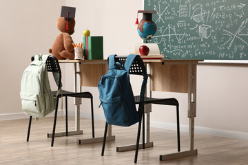 Desks with backpacks, graduation hats and toy in classroom