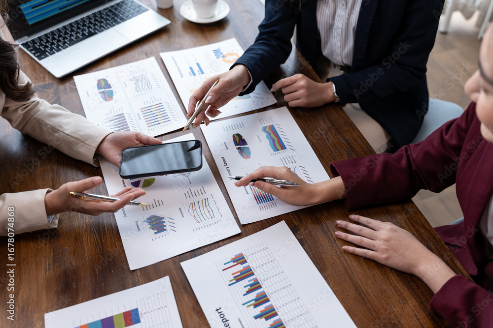 Poster team members review printed charts at a table, pointing with pens and a smartphone during a data-dri