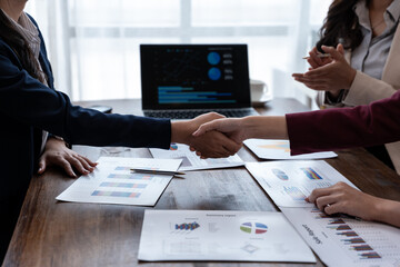 Business professionals shake hands over a table with charts and a laptop, sealing a deal during a...
