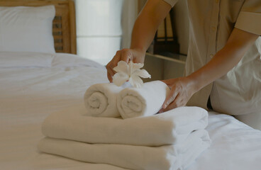 A housekeeper's hand is holding a white flower and placing it on a towel, preparing it for...