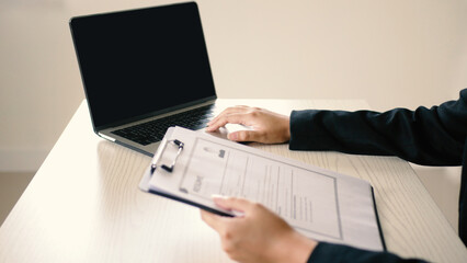 A young businesswoman is sitting and using a laptop to recruit new employees, looking at the resumes of several job applicants at the same time