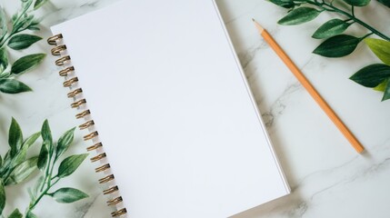 Blank spiral notebook and orange pencil on a marble surface surrounded by green leaves for creative inspiration