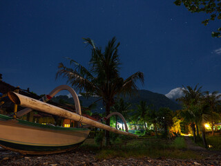 Night scenery from Amed, Bali – a traditional jukung fishing boat resting on the beach among palm...