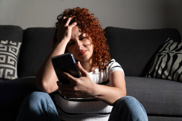 Stressed woman holding smartphone and touching head at home
