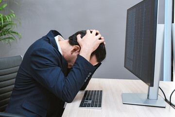 Young Businessman or Programmer looking worried and stressed over working on a computer code at...