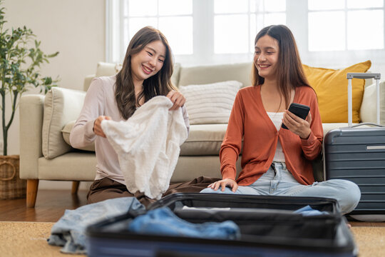 Young asian woman and friend preparing luggage packing clothes in suitcases for travel at home, planning holiday travel, content creator and travel blogger, friendship moments lifestyle vacation trip - Powered by Adobe