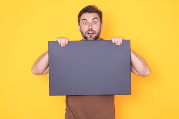 Amazed handsome man with blank banner ad isolated on studio background. Portrait of surprised man...