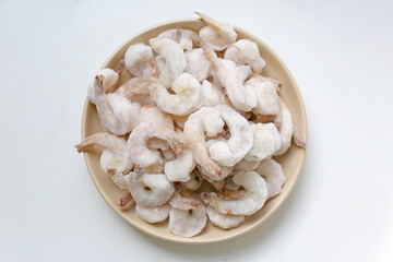 Frozen shrimps in a white bowl on wooden board.