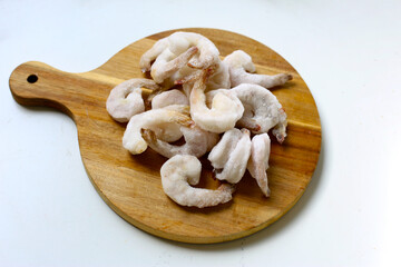 Frozen shrimps in a white bowl on wooden board.