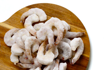 Frozen shrimps in a white bowl on wooden board.