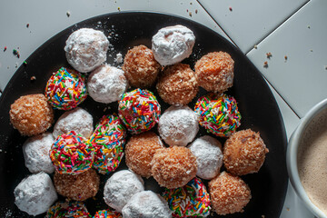 Sweet bread balls on a black plate with a cup of hot chocolate next to it. Concept of high-sugar carbohydrates and diabetes care.