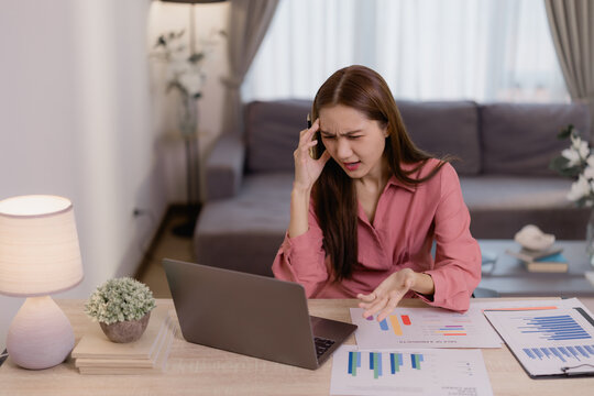 Young stressed asian businesswoman having headache and problems while talking on phone and working on laptop at home office, worried entrepreneur having financial problems during covid pandemic