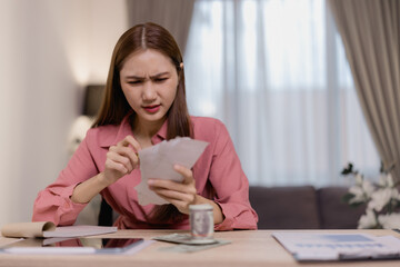Young worried asian businesswoman calculating domestic bills and managing monthly expenses sitting at her desk at home, struggling with financial problems, having debt and worried about bankruptcy