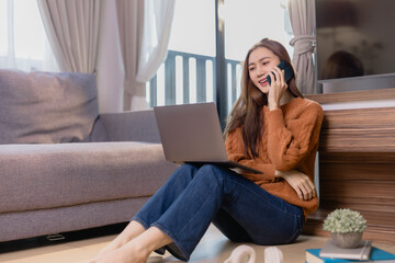 Freelancer is using her laptop and talking on the phone while working remotely from her living room, enjoying the comfort and flexibility of her home office
