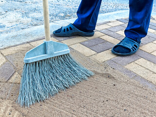 Person sweeping clean sand from a brick pavement in a residential area during daylight working hours