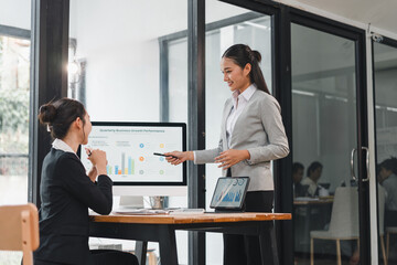Young professional woman presenting business growth chart to female colleague in modern office, confident and engaged in collaborative meeting