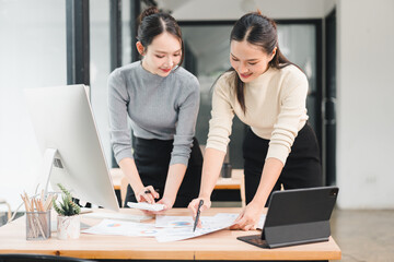 Fototapeta premium Young woman working on office documents with colleague, reviewing chart and pointing at paper, collaborative planning and focused discussion