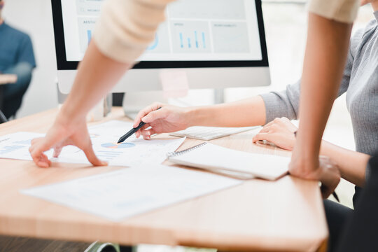 Young professional teamwork meeting discussing business chart and digital report with pen and notebook on office desk, collaborative planning and focused analysis