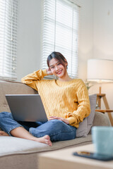 Young woman smiling on sofa with laptop wearing yellow sweater relaxed natural light cozy home scene