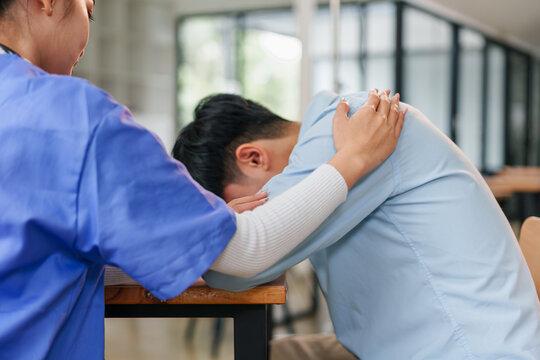 Young man with head down at table comforted by caregiver offering supportive embrace, emotional moment of compassion and care in indoor setting