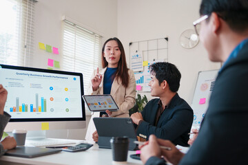 Young businesswoman presenting quarterly business growth performance to attentive colleagues modern office, using tablet and large screen with charts and collaborative notes showing focused