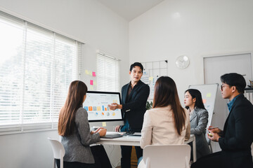 Young professional giving presentation to colleagues in modern office, discussing data charts and collaborative planning with engaged team members