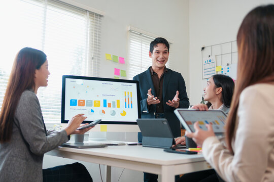 Young professional team meeting with presentation screen showing charts and graphs, collaborative discussion and digital devices in modern office, upbeat atmosphere