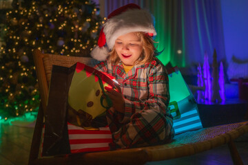 Cute child opening gift bag in room decorated for night Christmas. Happy little kids in matching...