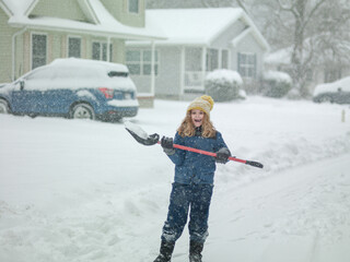 Child clearing sidewalks and shoveling snow. Child removing snow with shovel. Little helper. Winter...