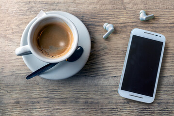 Cup of Coffee with Smartphone and Wireless Earbuds on Wooden Table