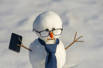 Snowman making a phone call with smartphone. Snow man using laptop outdoors in snow. Funny snowman businessman with mobile phone. Winter celebration with snowman. Hacker snowman.